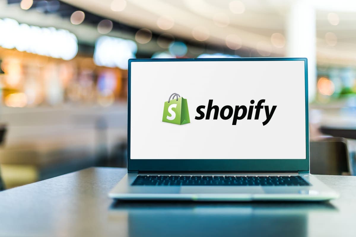 The Shopify logo on a laptop with a blurred background of a modern coworking space.